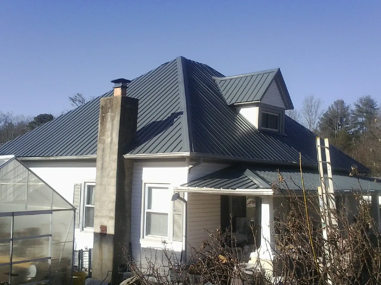 Dark blue standing seam metal roof on a white farmhouse with dormer — Slate & Tile Roof Repair by Roofing Brothers in Hot Springs