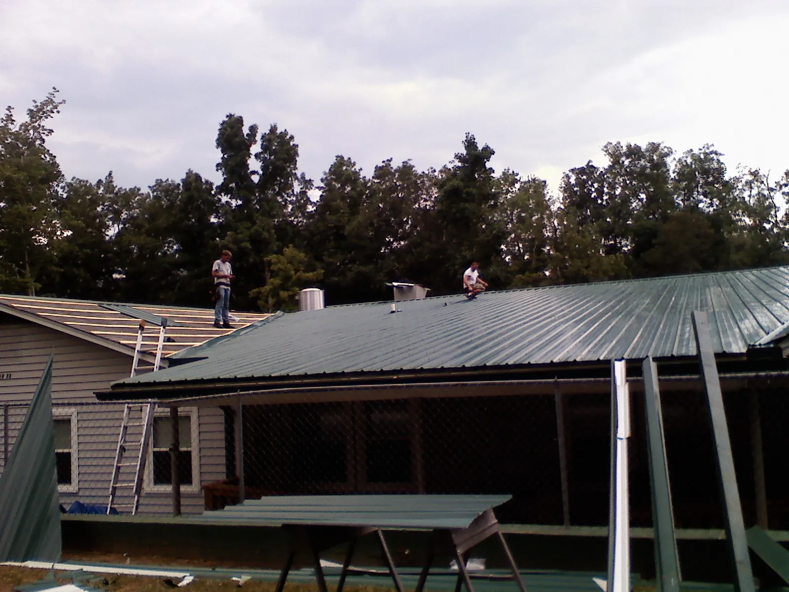 Two roofers installing green metal panels above a covered porch in Hot Springs